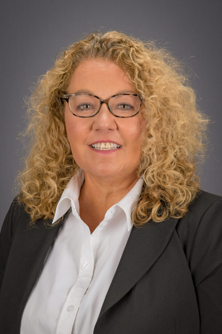 A woman with blonde hair and glasses in a black suit.